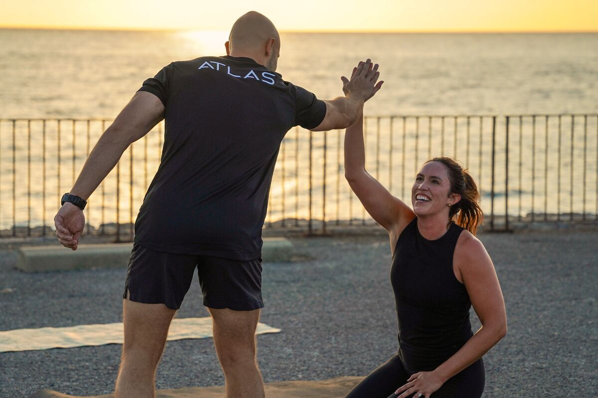 A coach high-fiving a client on the seafront at sunrise