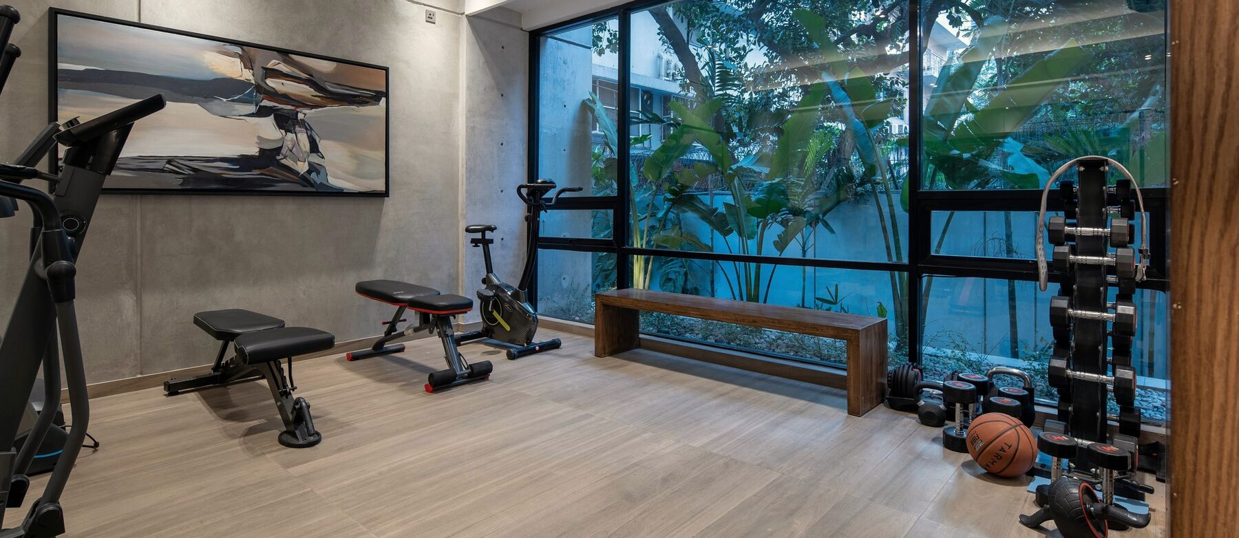A private gym in a villa, with a bench, a bike and dumbbells beside a garden window